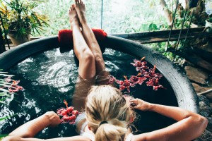 Woman relaxing in round outdoor bath with tropical flowers. Organic skin care in kawa hot bath in luxury spa resort.